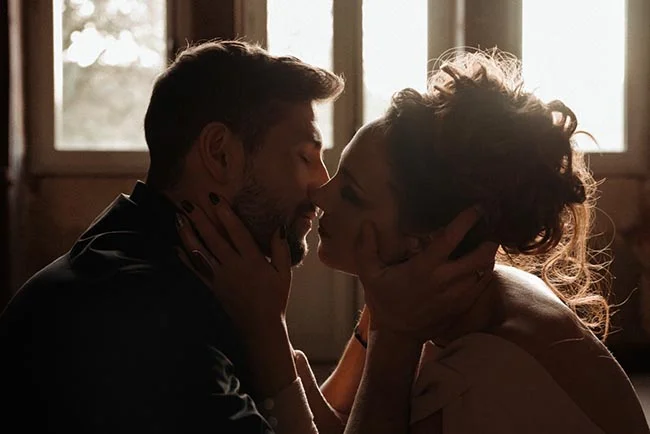Couple de mariés s'embrassant avec tendresse dans un jeu de contre-jour chaleureux et romantique.