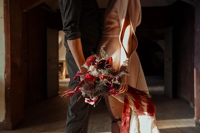 Couple en tenue élégante tenant un bouquet rouge et sombre dans un jeu de contrastes d'ombre et de lumière.