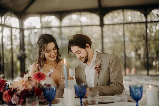 Jeunes mariés souriants à une table décorée de fleurs et bougies, dans une ambiance romantique et lumineuse.