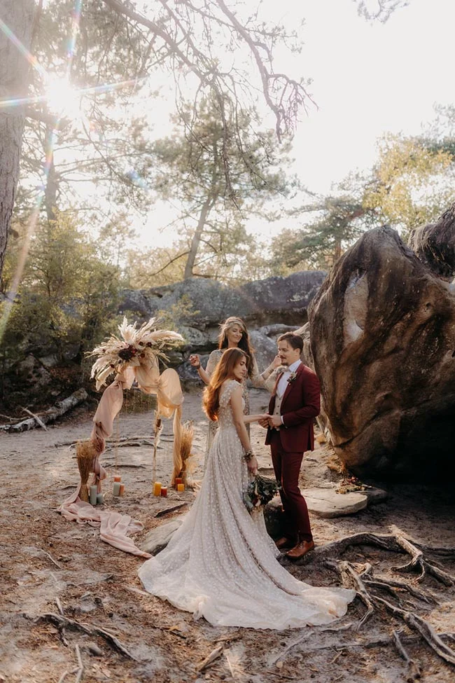 Couple d'élopement en tenue de mariage devant une arche bohème, dans un décor naturel et rocheux et lumineux.