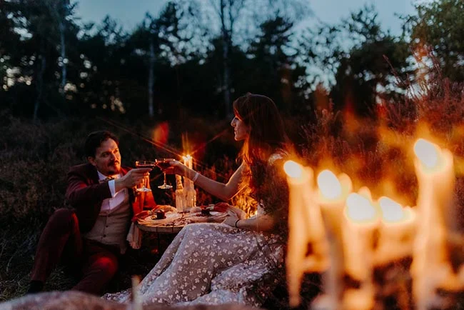 Couple en tenue de mariage trinquant aux chandelles lors d'un dîner romantique en plein air au crépuscule.