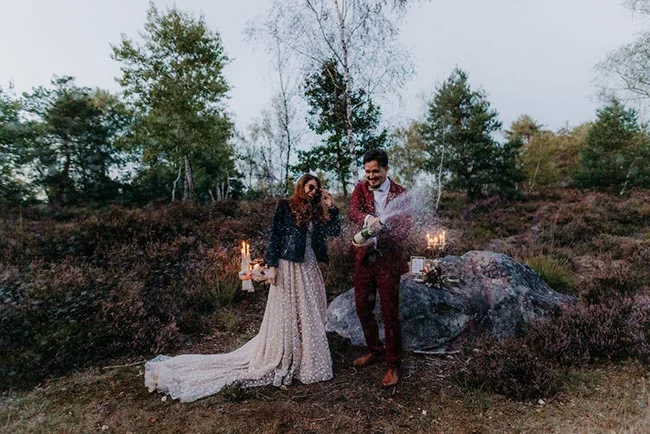 Couple en tenue de mariage célébrant un elopement en pleine nature avec du champagne et des bougies.