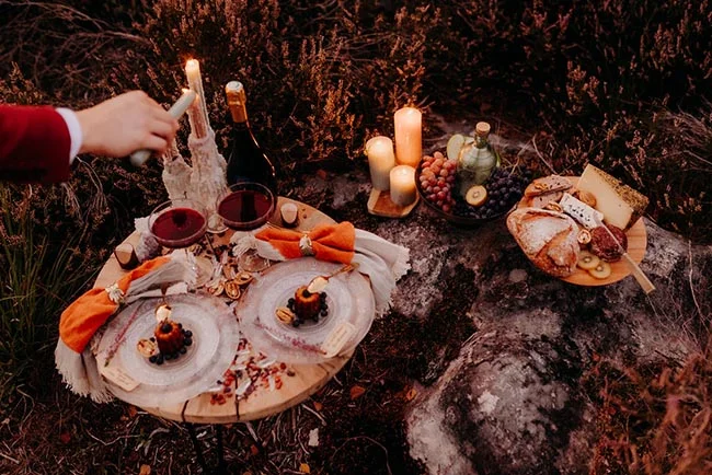 Pique-nique romantique et chaleureux en pleine nature avec vin, fromage et bougies à la lueur du crépuscule.