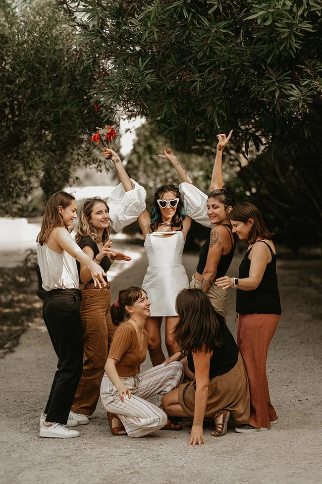 Une mariée et ses demoiselles d'honneur rient et s'amusent avec enthousiasme sous un grand arbre verdoyant.