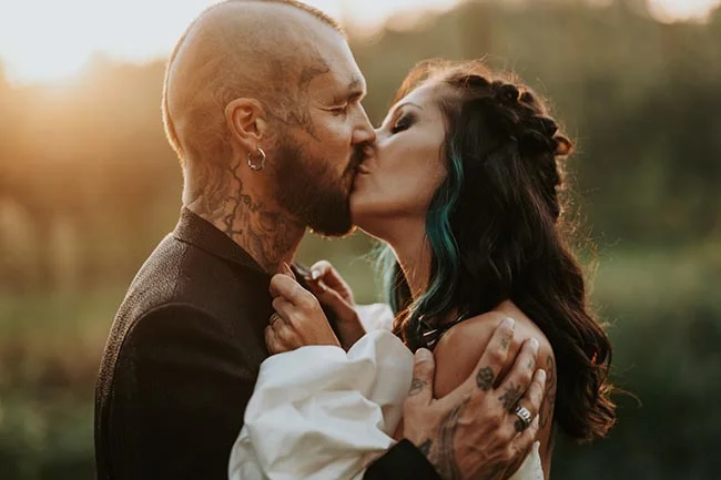 Couple tatoué s'embrassant avec passion lors d'un mariage alternatif, ambiance chaleureuse et lumière dorée.