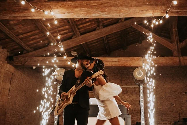 Couple s'embrassant avec passion sous des étincelles, l'homme jouant de la guitare dans une grange rustique et chaleureuse.