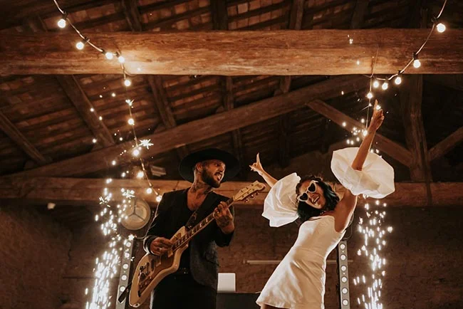 Couple festif dans une grange rustique avec guitare et feux d'artifice, ambiance chaleureuse et dynamique.