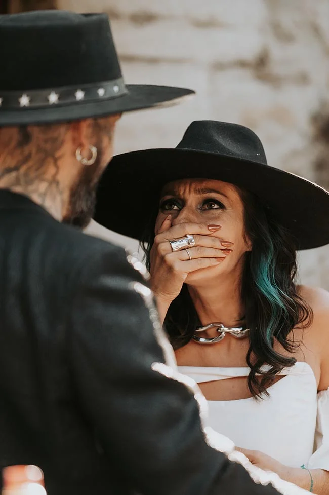 Couple stylé en chapeaux noirs, la mariée surprise et émue, dans une ambiance moderne et audacieuse.