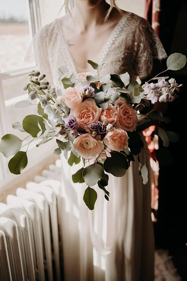 Mariée en robe de dentelle blanche tenant un bouquet romantique de roses poudrées et d'eucalyptus.