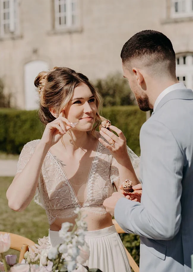 Jeunes mariés complices partageant des mignardises dans un jardin, ambiance romantique et lumineuse.