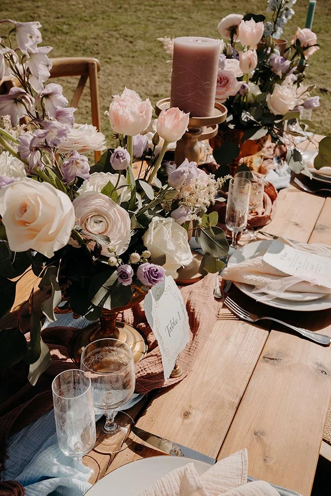 Décoration de table romantique avec compositions florales pastel, bougie et art de la table sur bois naturel.
