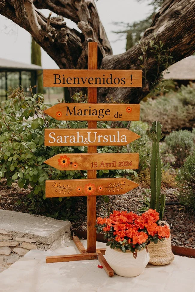 Panneau directionnel en bois pour le mariage de Sarah et Ursula, décoré de fleurs orange dans un style folk mexicain.