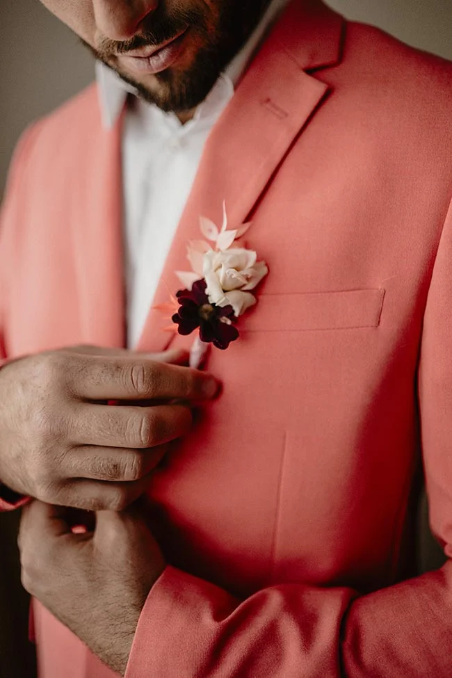 Gros plan d'un marié en costume corail avec une boutonnière fleurie pour un mariage moderne et coloré.
