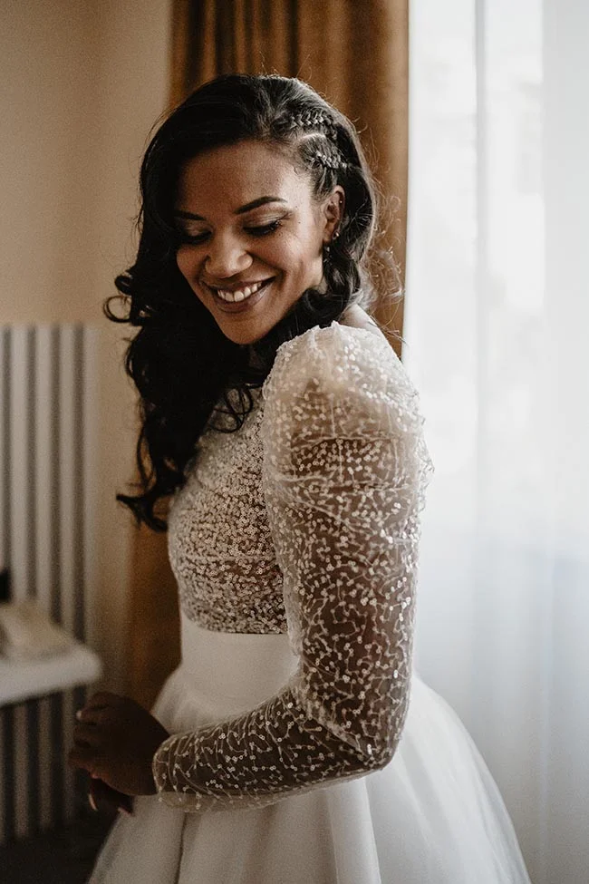 Mariée souriante en robe blanche à sequins scintillants, ambiance lumineuse et romantique.