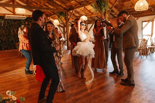 Invités festifs et mariée en robe courte dansant dans une salle rustique en bois à l'ambiance décontractée.
