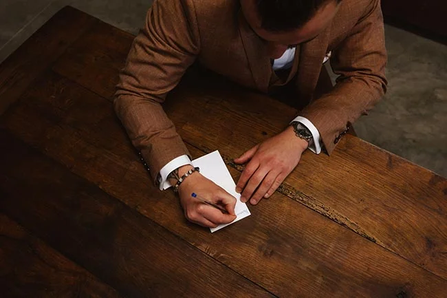 Gros plan d'un marié en costume marron écrivant une lettre sur une table en bois rustique.