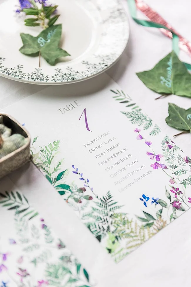 Plan de table floral et élégant avec feuillage naturel sur une nappe blanche, ambiance mariage forêt enchantée.