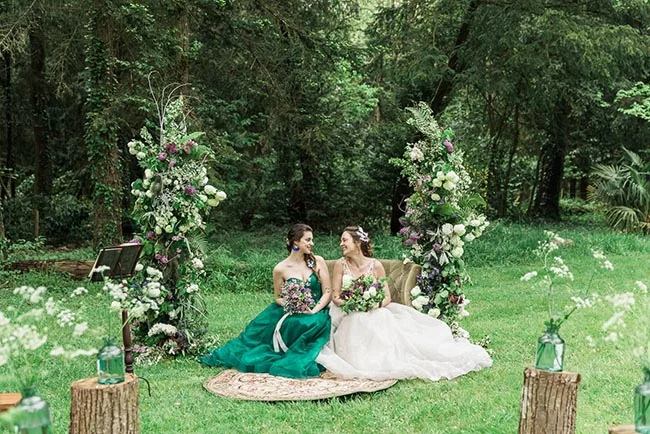 Deux mariées assises dans une forêt enchantée, entourées de compositions florales et d'une nature verdoyante.