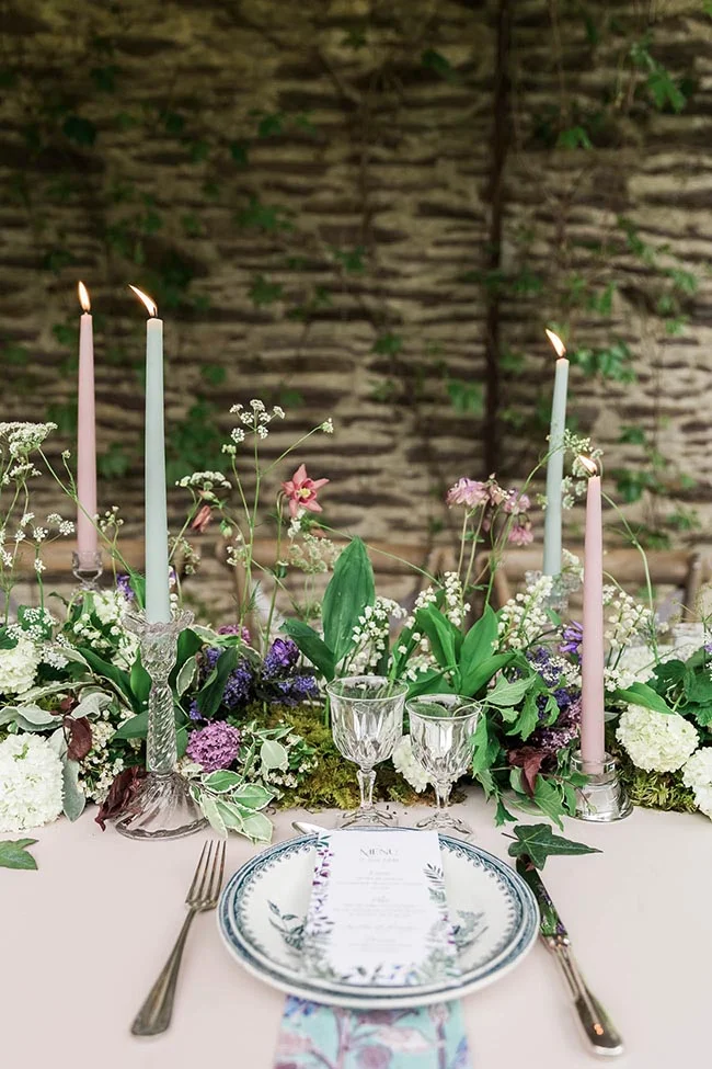 Décoration de table romantique avec bougies pastel, fleurs sauvages et vaisselle élégante dans un esprit forêt enchantée.