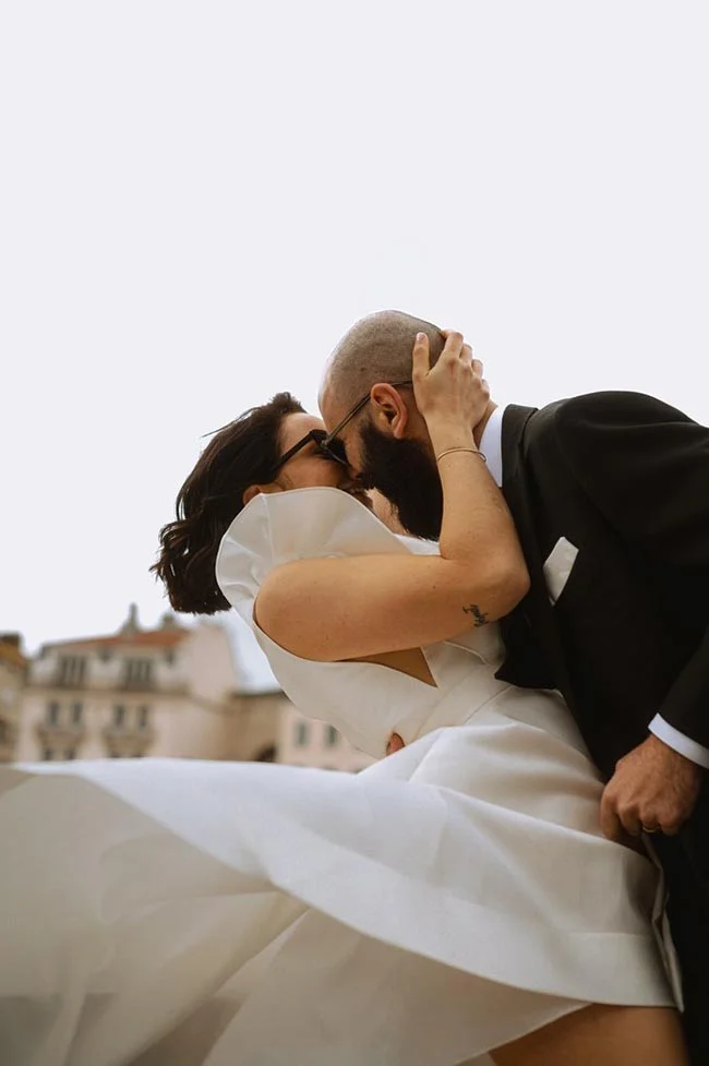 Couple élégant s'embrassant avec passion, la mariée en robe blanche fluide et le marié en costume noir chic.