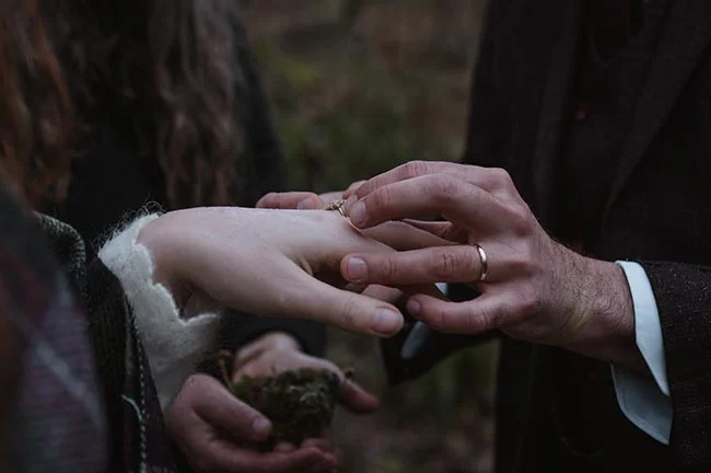 Gros plan sur un homme glissant une bague au doigt d'une femme dans une ambiance sombre et romantique.