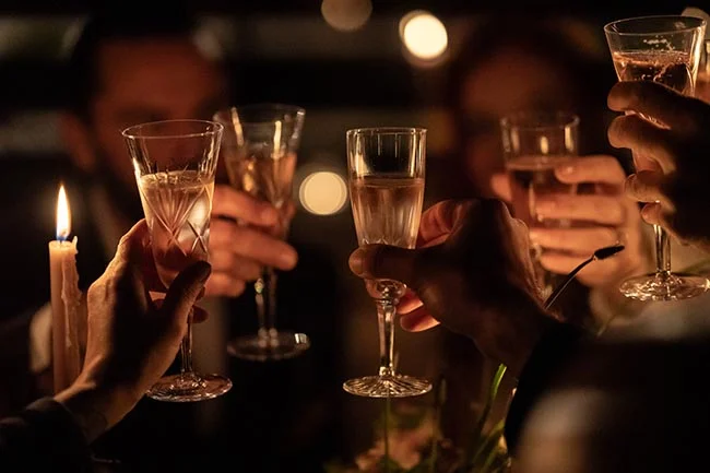 Quatre mains trinquant avec des coupes de champagne à la lueur d'une bougie dans une ambiance intime et tamisée.