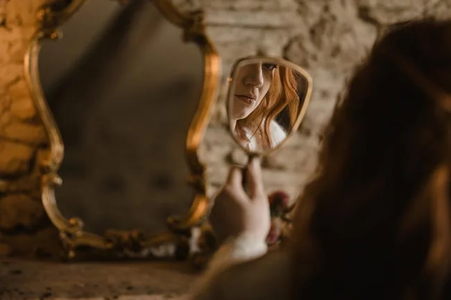 Gros plan d'une femme se regardant dans un petit miroir à main, ambiance chaleureuse et tons dorés.