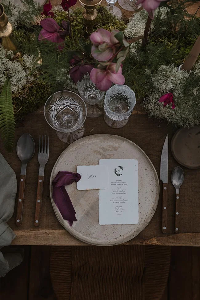Dressage de table rustique et romantique avec menu, fleurs roses et mousse végétale dans des tons naturels.