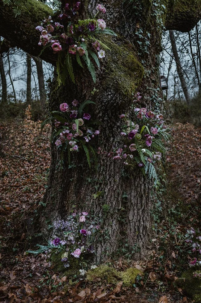 Composition florale romantique aux tons mauves et roses ornant le tronc moussu d'un vieil arbre en forêt.