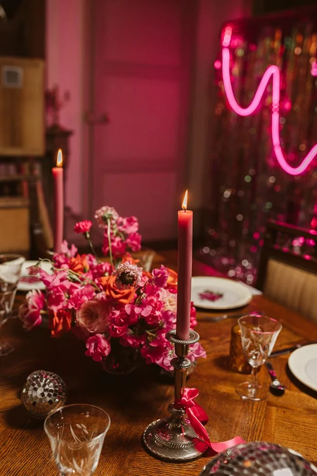 Table festive avec fleurs roses, bougies allumées et néon rose pour une ambiance d'EVJF pétillante et moderne.