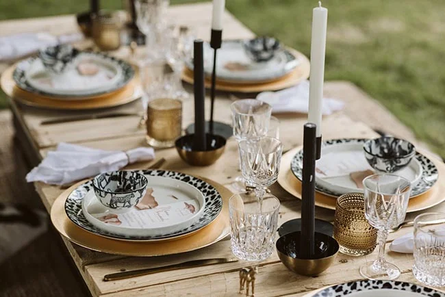 Table dressée avec élégance pour un EVJF, mêlant vaisselle graphique noire et blanche, touches dorées et bougies.