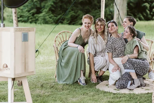 Quatre amies souriantes et élégantes posent ensemble en extérieur lors d'un EVJF dans des tons neutres et vert olive.