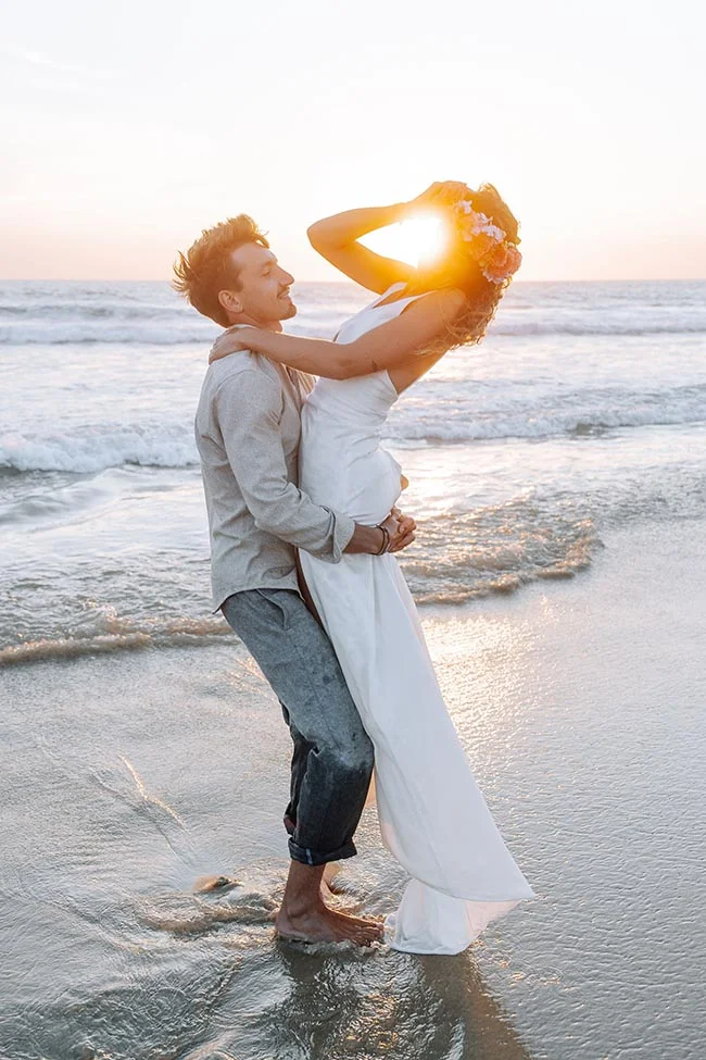 Couple de mariés s'enlaçant sur une plage au coucher du soleil, ambiance romantique et lumineuse.