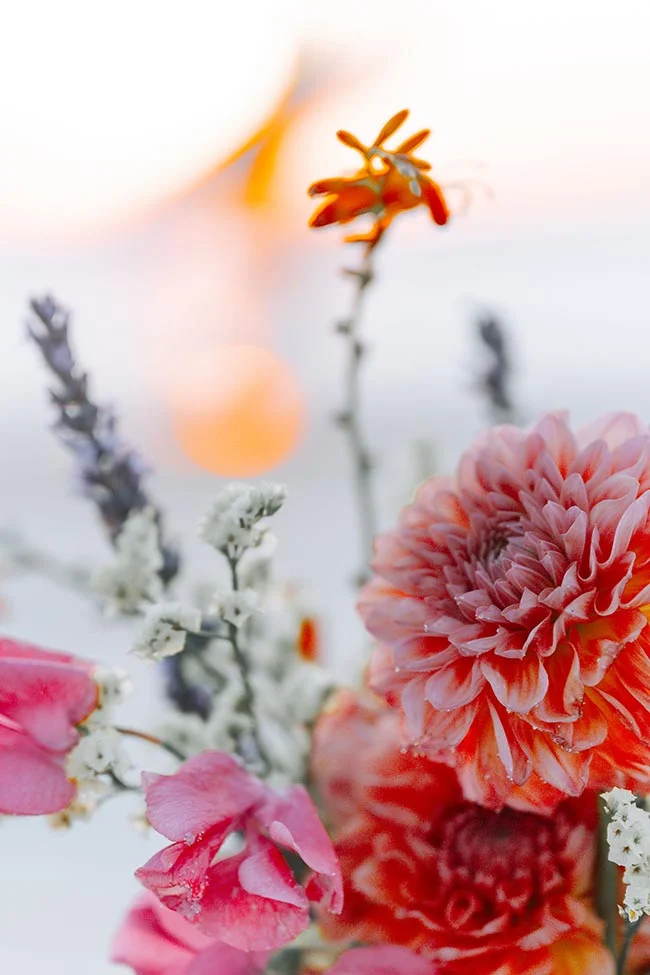 Gros plan flou et lumineux d'un bouquet de fleurs colorées dans des tons rose, orange et blanc pour un mariage à la plage.