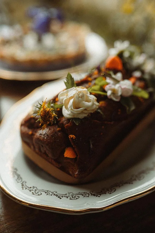 Gâteau au chocolat décoré de fleurs blanches et jaunes sur une assiette élégante, ambiance rustique et chaleureuse.