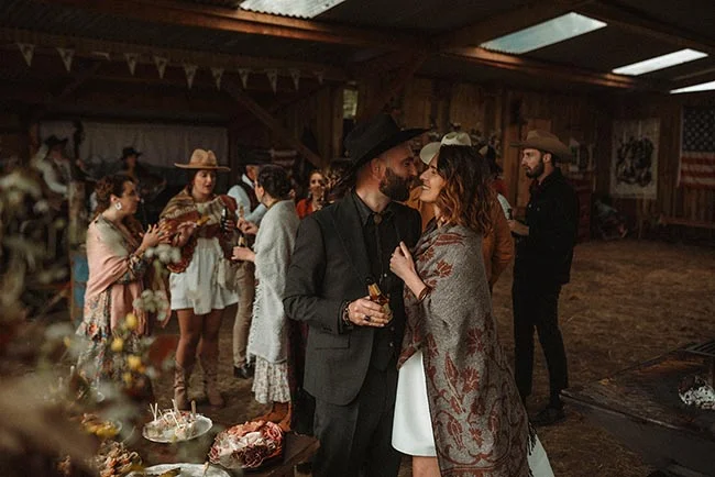 Couple élégant en tenue western discutant lors d'une réception champêtre et chaleureuse dans une grange.