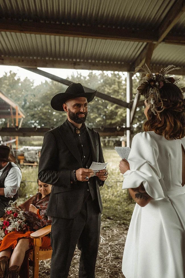 Un couple s'échange ses vœux lors d'un mariage western, le marié portant un costume noir et un chapeau de cowboy.