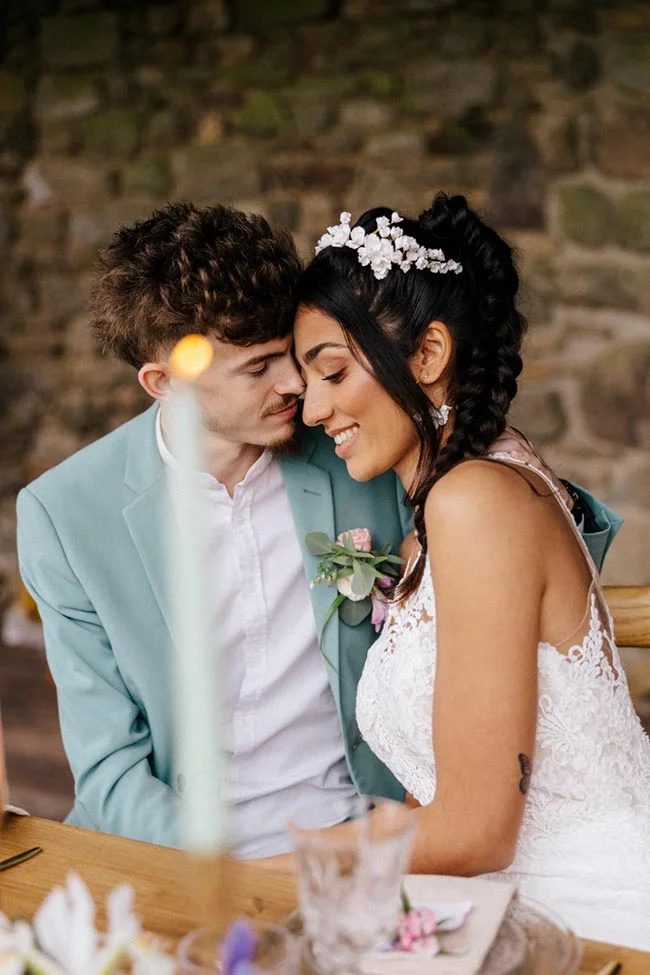Jeunes mariés complices, elle en robe blanche et lui en costume bleu clair, dans un cadre rustique et romantique.