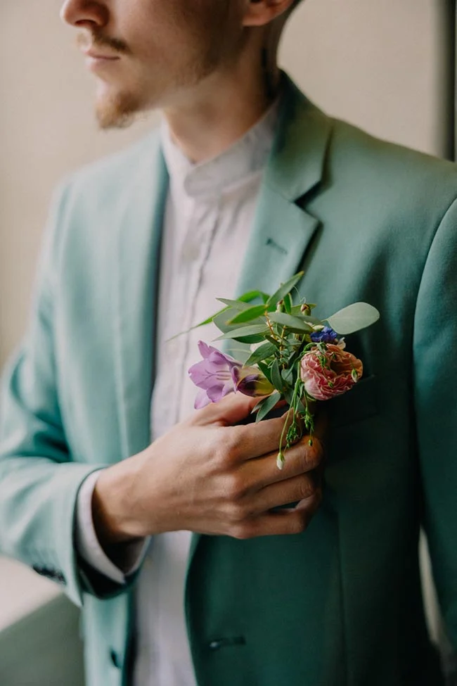 Gros plan d'un homme en costume vert d'eau portant une boutonnière fleurie colorée.