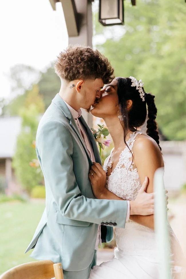Jeune couple de mariés s'embrassant tendrement, elle en robe blanche et lui en costume bleu clair, ambiance romantique.