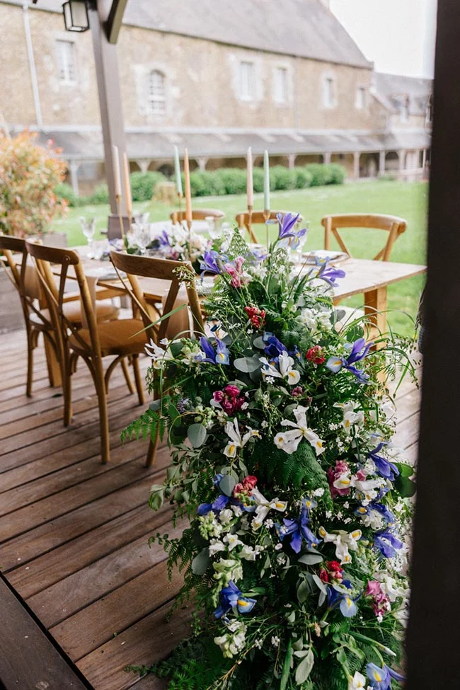 Table de réception en bois avec compositions florales champêtres et colorées sur une terrasse en Bretagne.