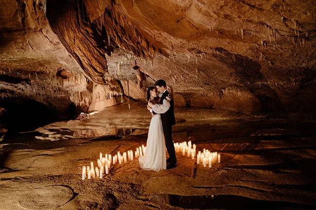 Couple de mariés s'enlaçant dans une grotte éclairée à la bougie, ambiance romantique et chaleureuse aux tons ocres.