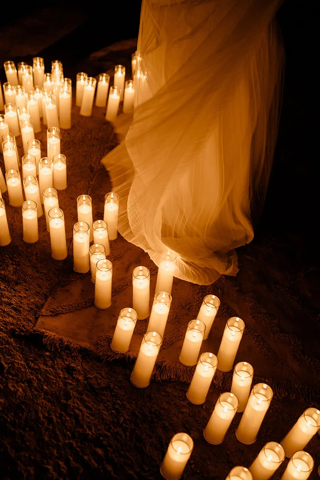 Nombreuses bougies allumées entourant le bas d'une robe de mariée vaporeuse dans une ambiance chaleureuse et romantique.