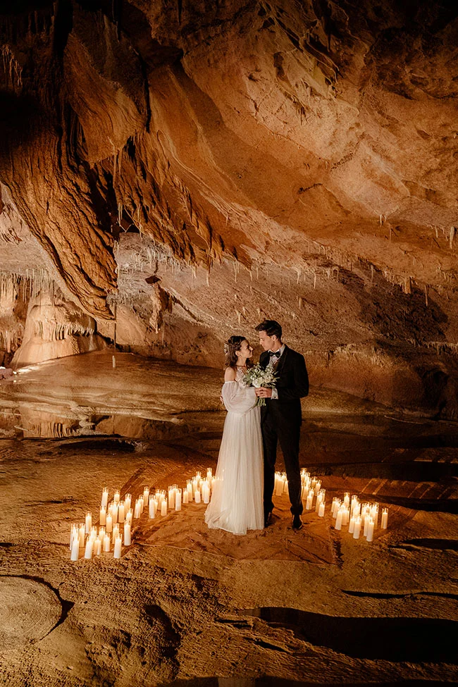 Couple de mariés s'enlaçant dans une grotte éclairée à la bougie, ambiance romantique et chaleureuse aux tons ocres.