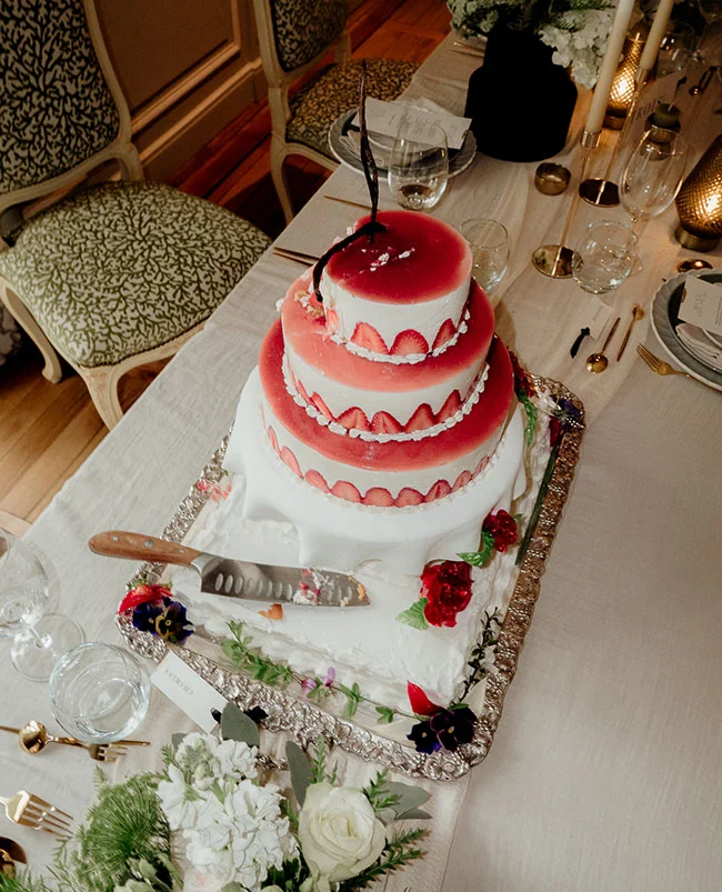 Gâteau de mariage à trois étages aux fraises et glaçage blanc, posé sur un plateau argenté lors d'une réception élégante.