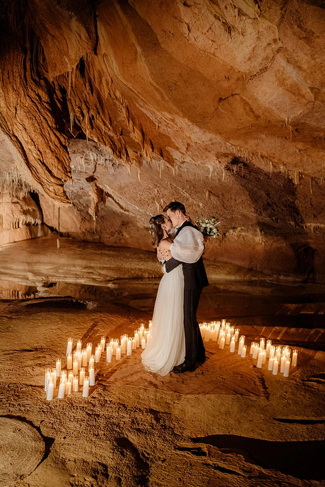 Jeunes mariés s'embrassant dans une grotte éclairée à la bougie, ambiance romantique et chaleureuse aux tons ocres.