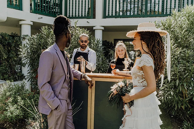 Couple élégant en tenue de mariage discutant avec un serveur lors d'une réception en plein air et lumineuse.