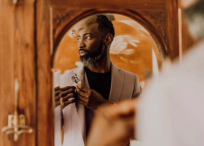 Homme élégant au reflet miroir, portant un costume clair et une boutonnière, dans une ambiance chaleureuse et jazzy.