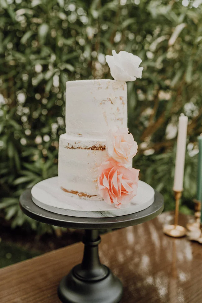 Gâteau de mariage blanc à étages, style semi-nu, décoré de roses poudrées sur un support noir élégant.