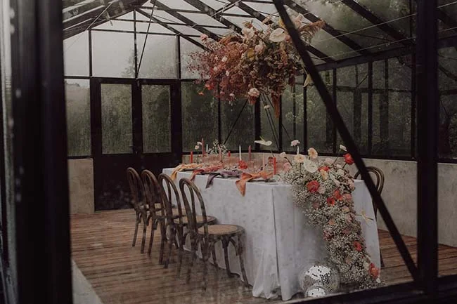 Table élégante dressée dans une serre avec compositions florales romantiques et bougies pour un mariage rétro.